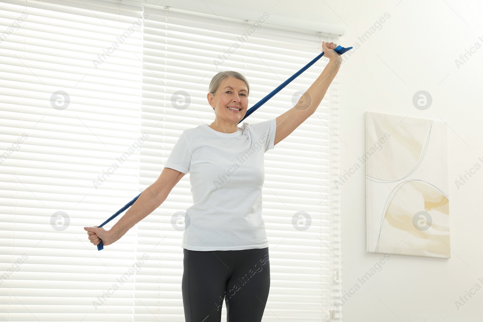 Photo of Senior woman doing exercise with fitness elastic band at home