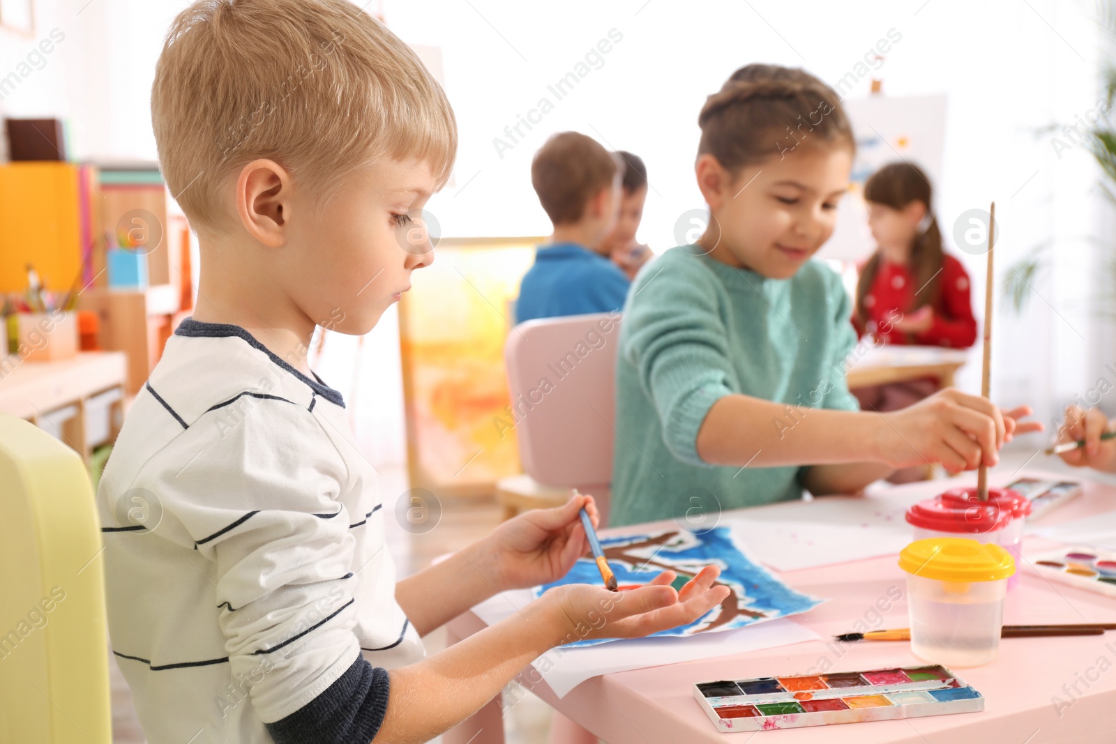 Photo of Cute little children painting their palms at table in room