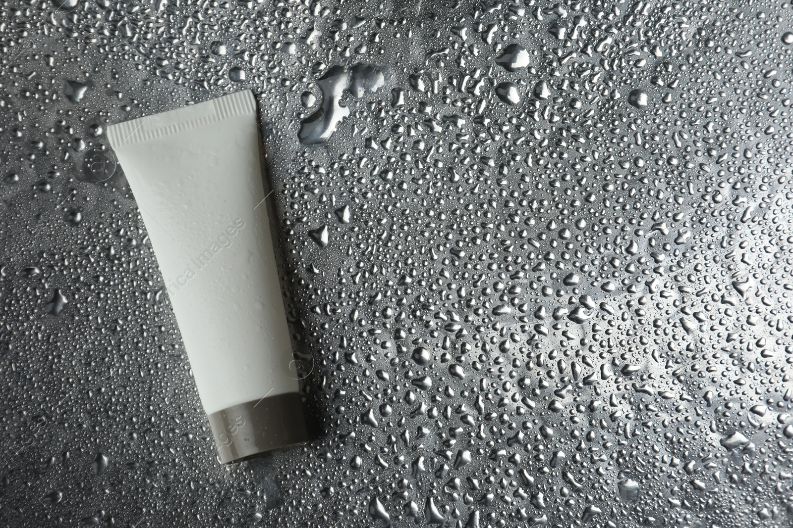Photo of Moisturizing cream in tube on silver background with water drops, top view. Space for text