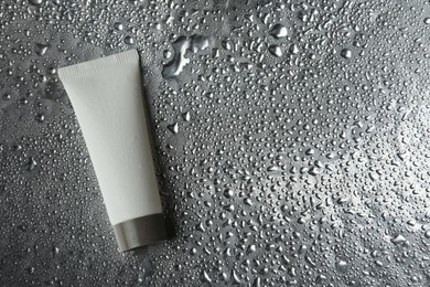 Photo of Moisturizing cream in tube on silver background with water drops, top view. Space for text