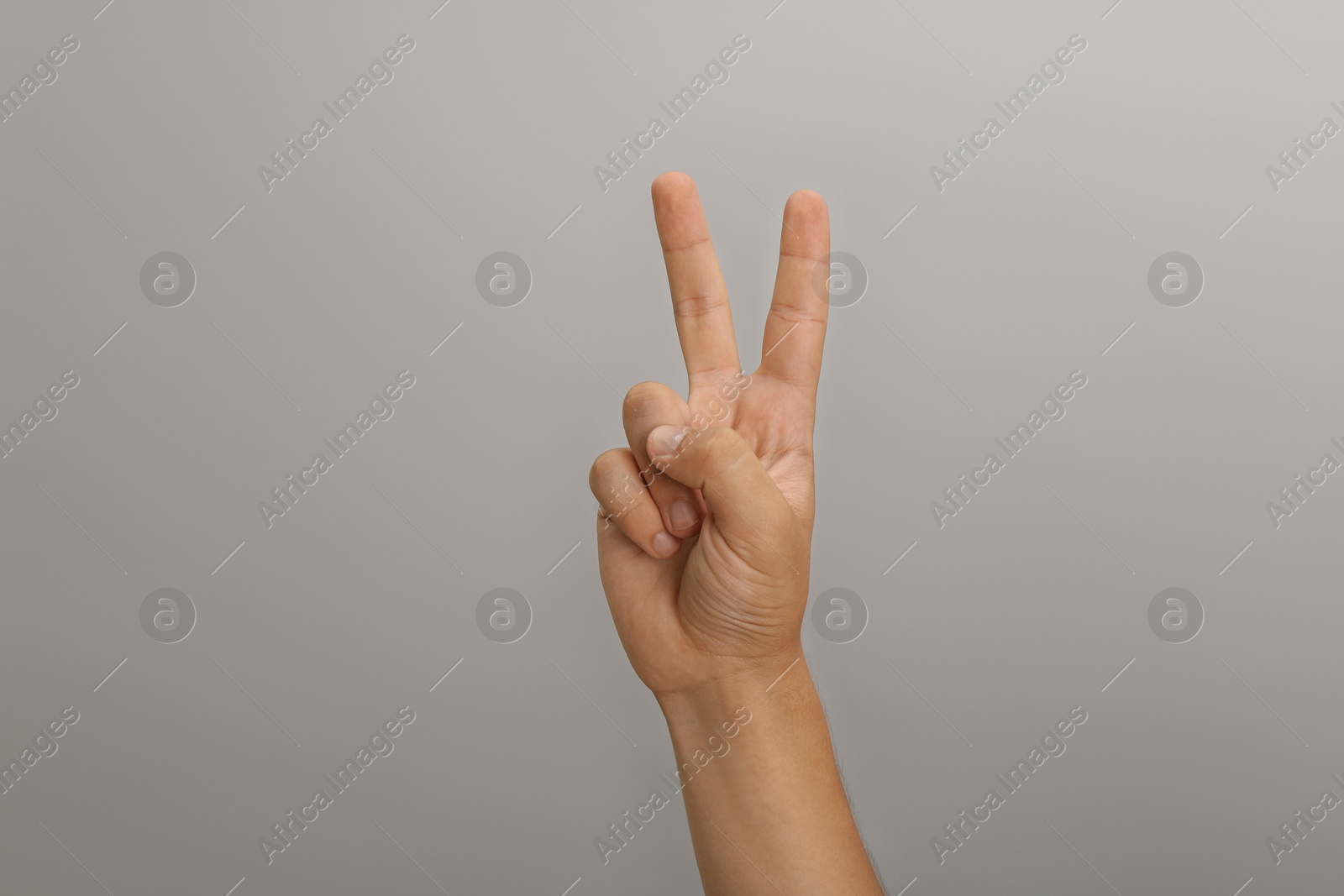 Photo of Teenage boy showing two fingers on light grey background, closeup