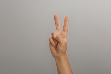Photo of Teenage boy showing two fingers on light grey background, closeup