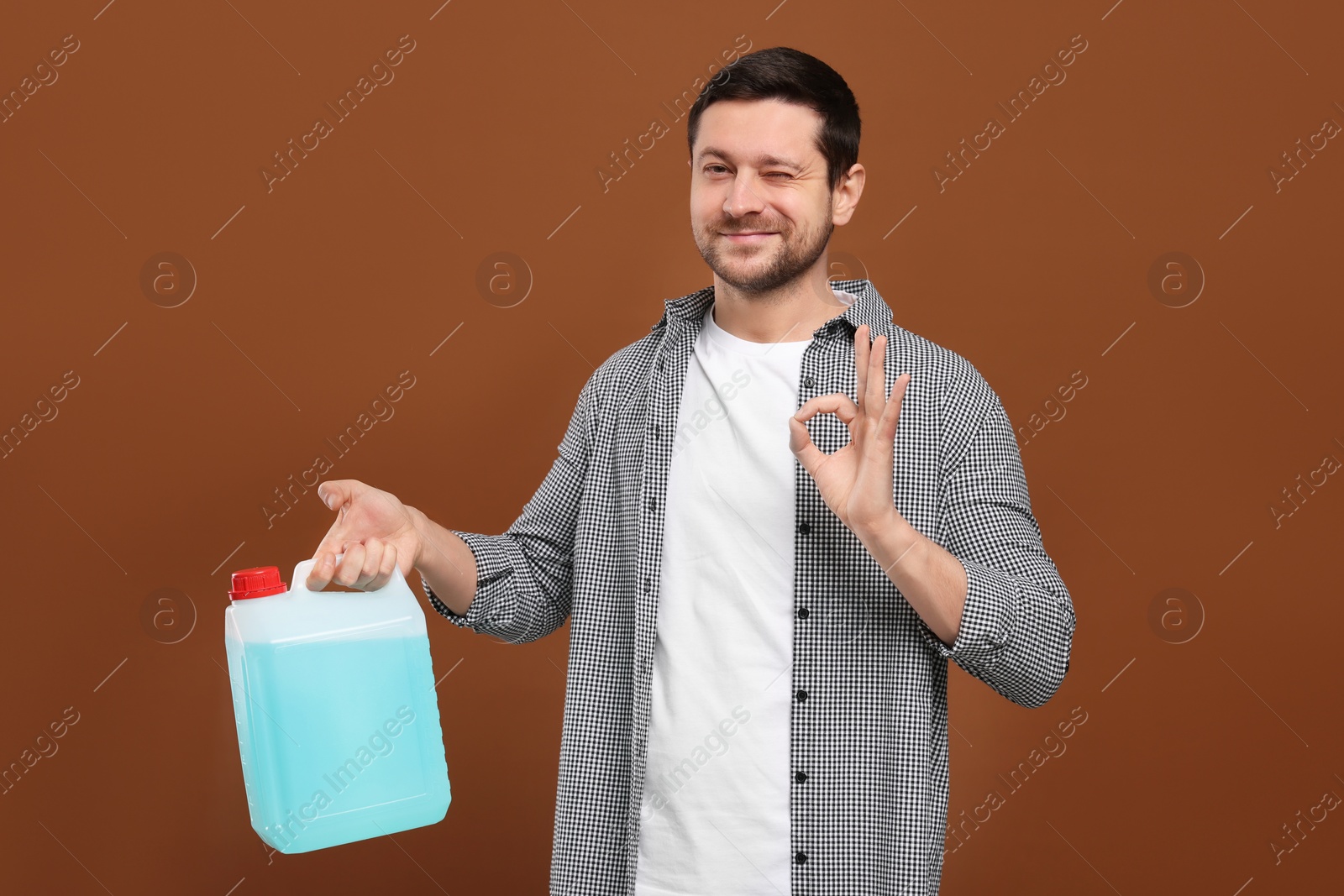 Photo of Man holding canister with blue liquid and showing OK gesture on brown background