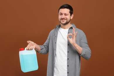 Man holding canister with blue liquid and showing OK gesture on brown background
