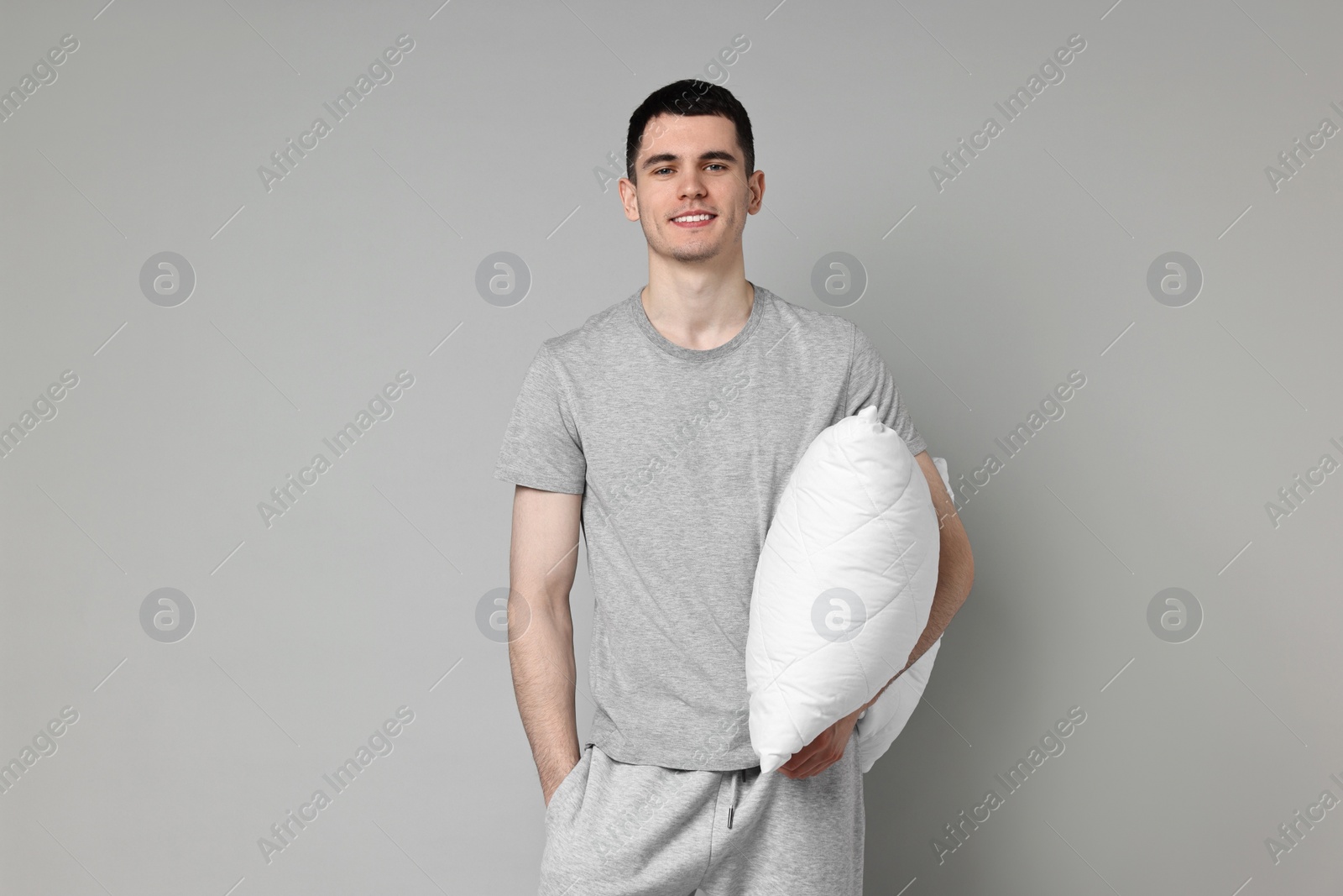 Photo of Happy man in pyjama holding pillow on grey background