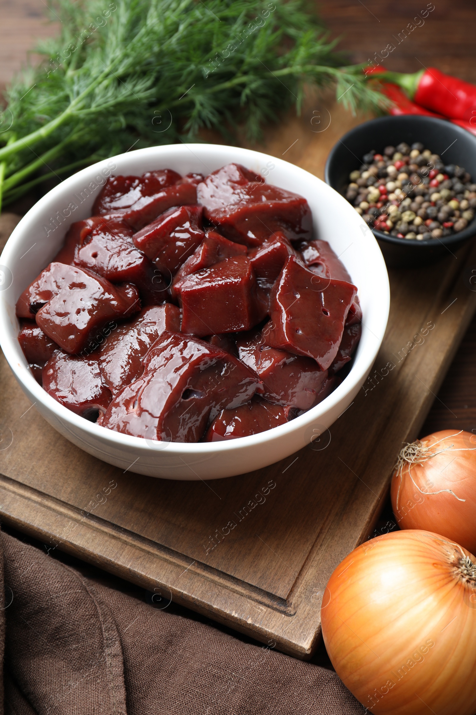 Photo of Cut raw beef liver with onions, dill and spices on wooden table