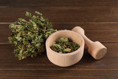 Photo of Mortar and pestle with dry parsley on wooden table