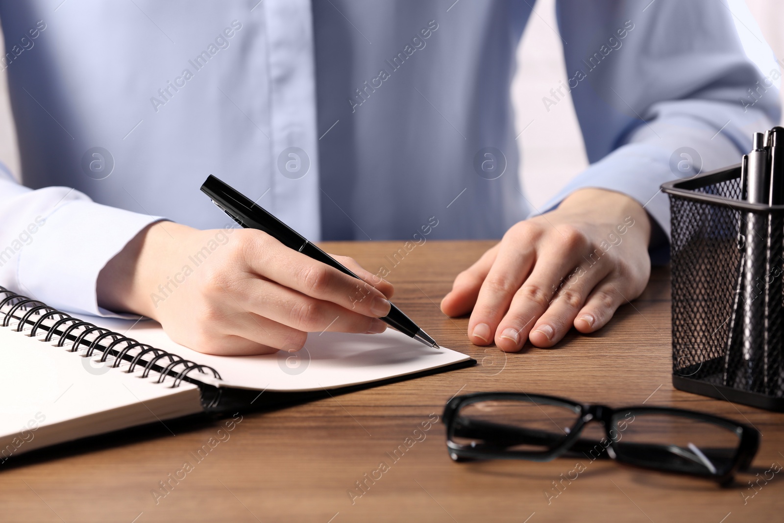 Photo of Woman writing in notebook at wooden table, closeup