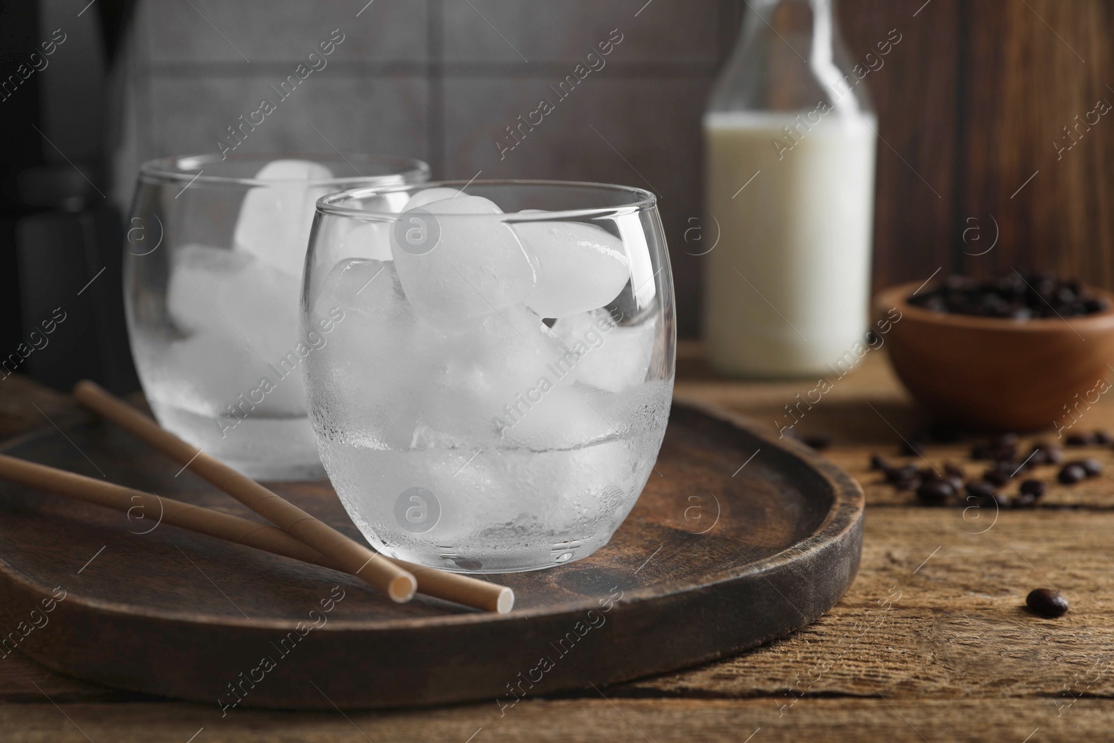 Photo of Making iced coffee. Ice cubes in glasses and straws on wooden table, closeup