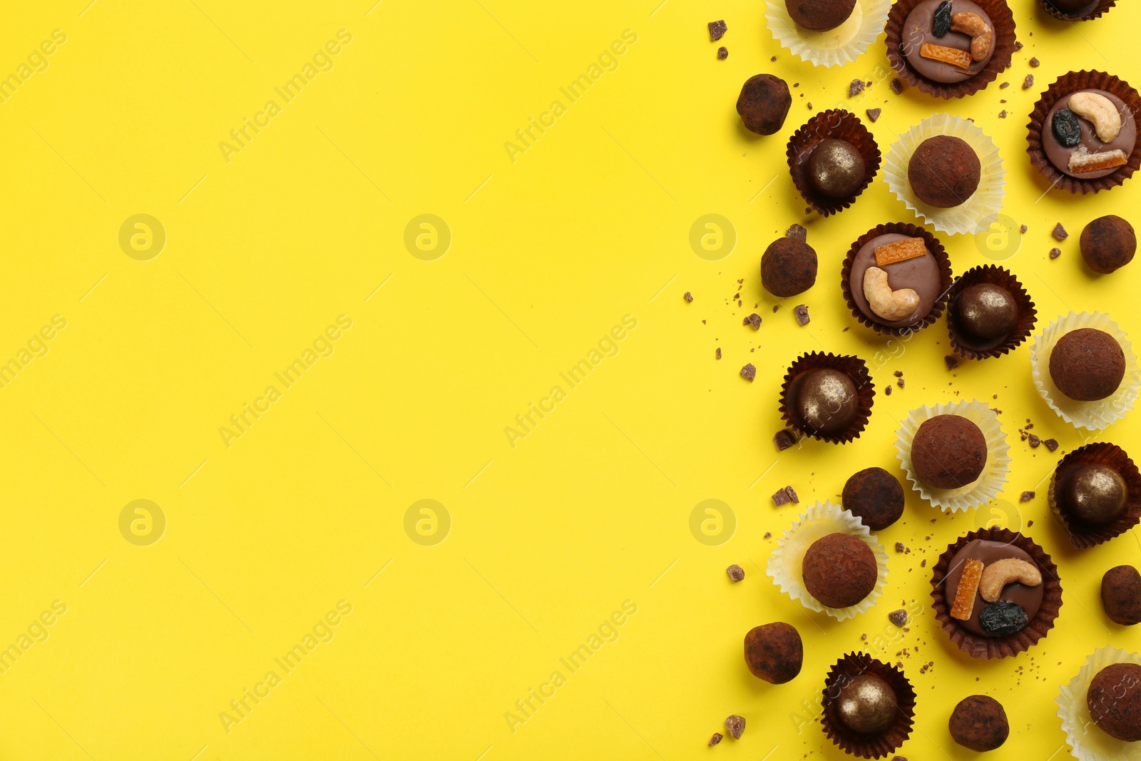 Photo of Different delicious chocolate candies on yellow background, flat lay. Space for text