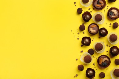 Different delicious chocolate candies on yellow background, flat lay. Space for text