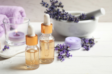 Composition with bottles of essential oil and lavender flowers on white wooden table