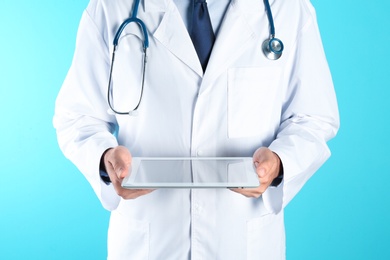 Male doctor holding modern tablet on color background, closeup