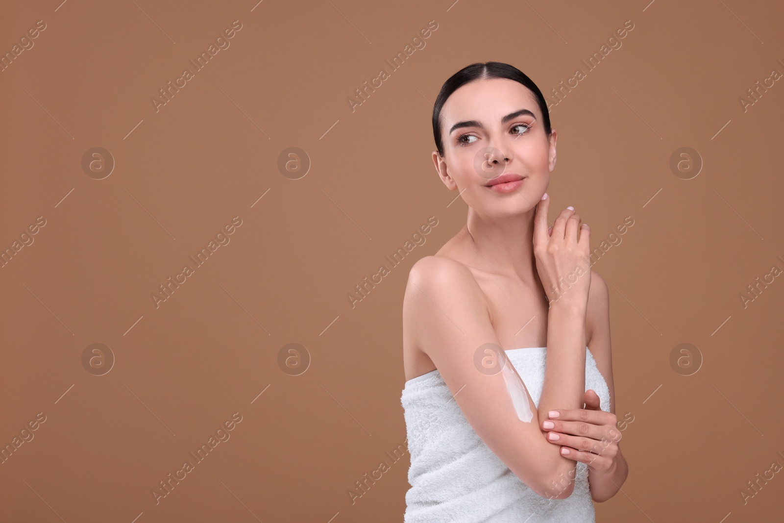 Photo of Beautiful woman with smear of body cream on her arm against light brown background, space for text