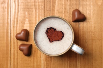 Cup of aromatic coffee with heart shaped decoration and chocolate candies on wooden table, flat lay