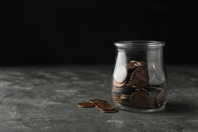 Glass jar with coins on grey table, space for text