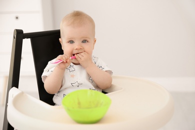 Photo of Cute little baby eating in high chair at home