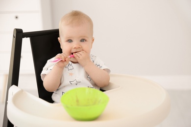 Cute little baby eating in high chair at home