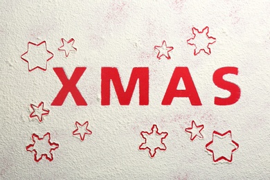 Photo of Word XMAS and snowflakes made of flour on red background, top view