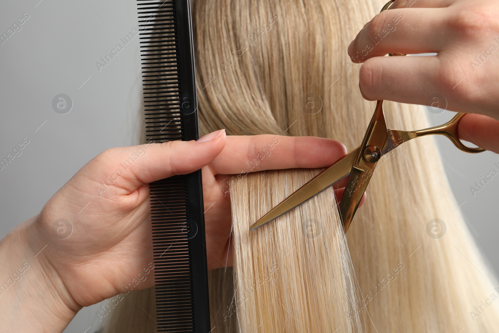 Photo of Hairdresser cutting client's hair with scissors on light grey background, closeup