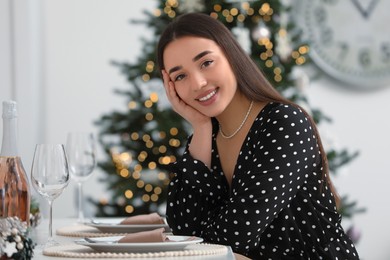 Portrait of happy woman sitting at table near Christmas tree indoors