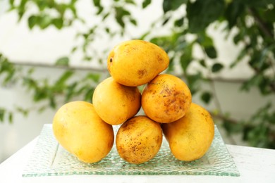 Photo of Delicious ripe yellow mangoes on glass plate outdoors