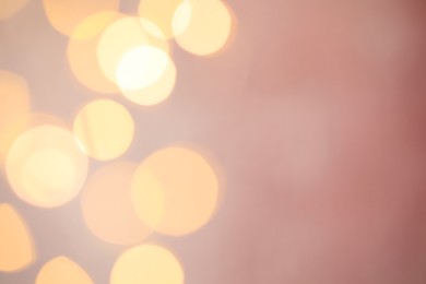 Blurred view of gold lights on pink background, bokeh effect. Space for text