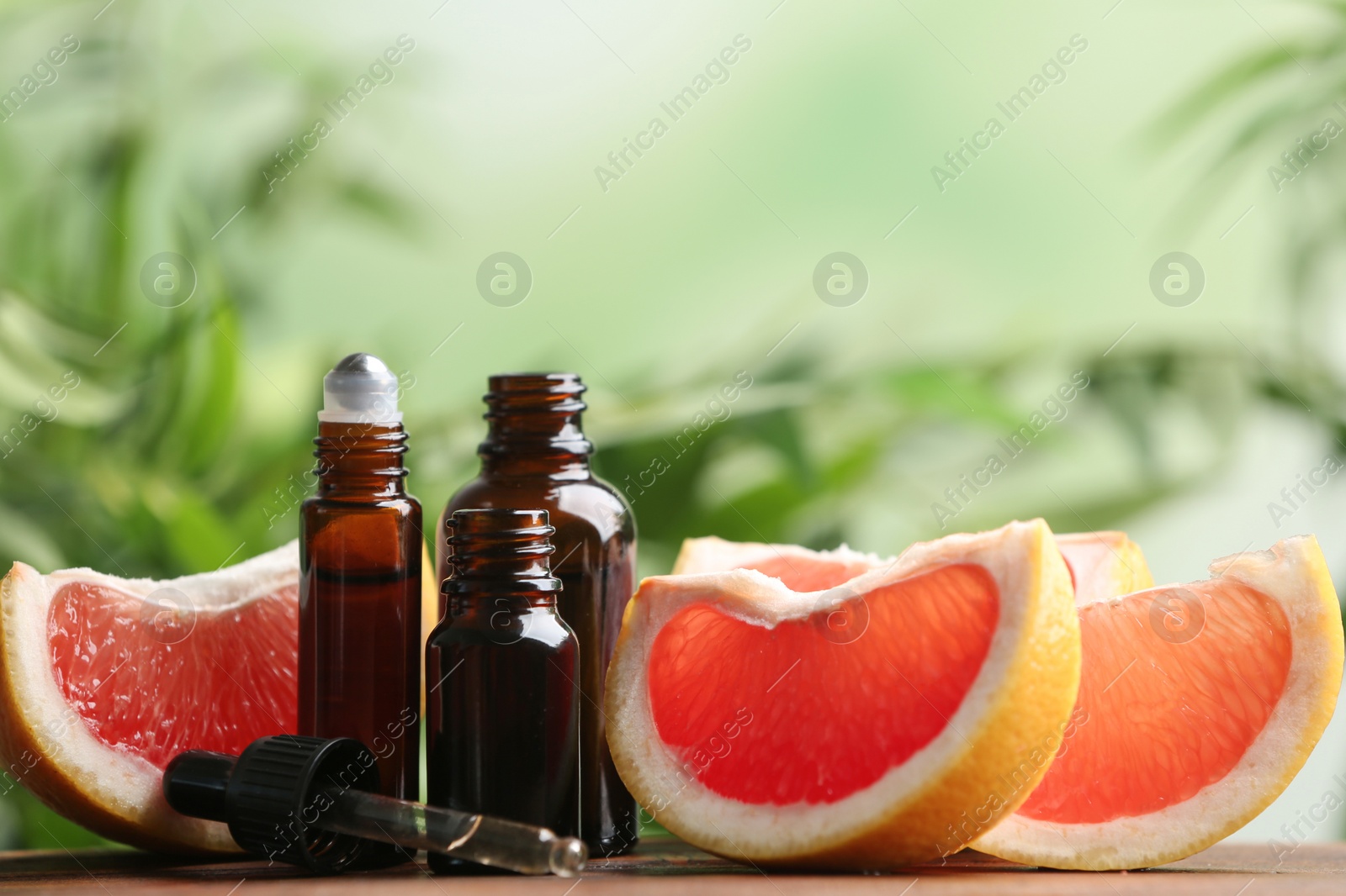 Photo of Bottles of essential oil and grapefruit slices on table against blurred background