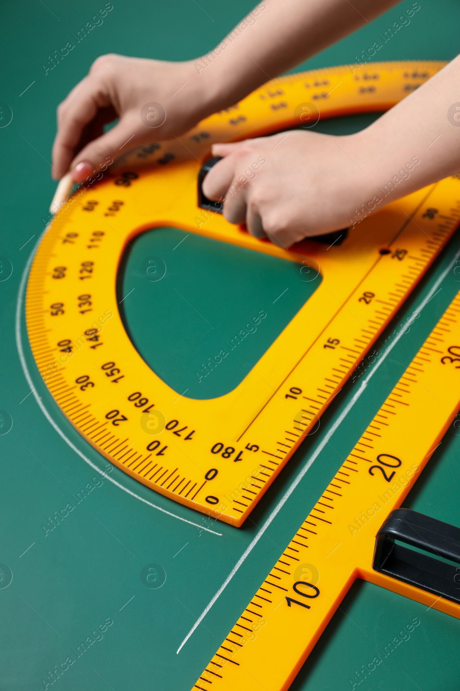 Photo of Woman drawing with chalk, triangle ruler and protractor on green board, closeup