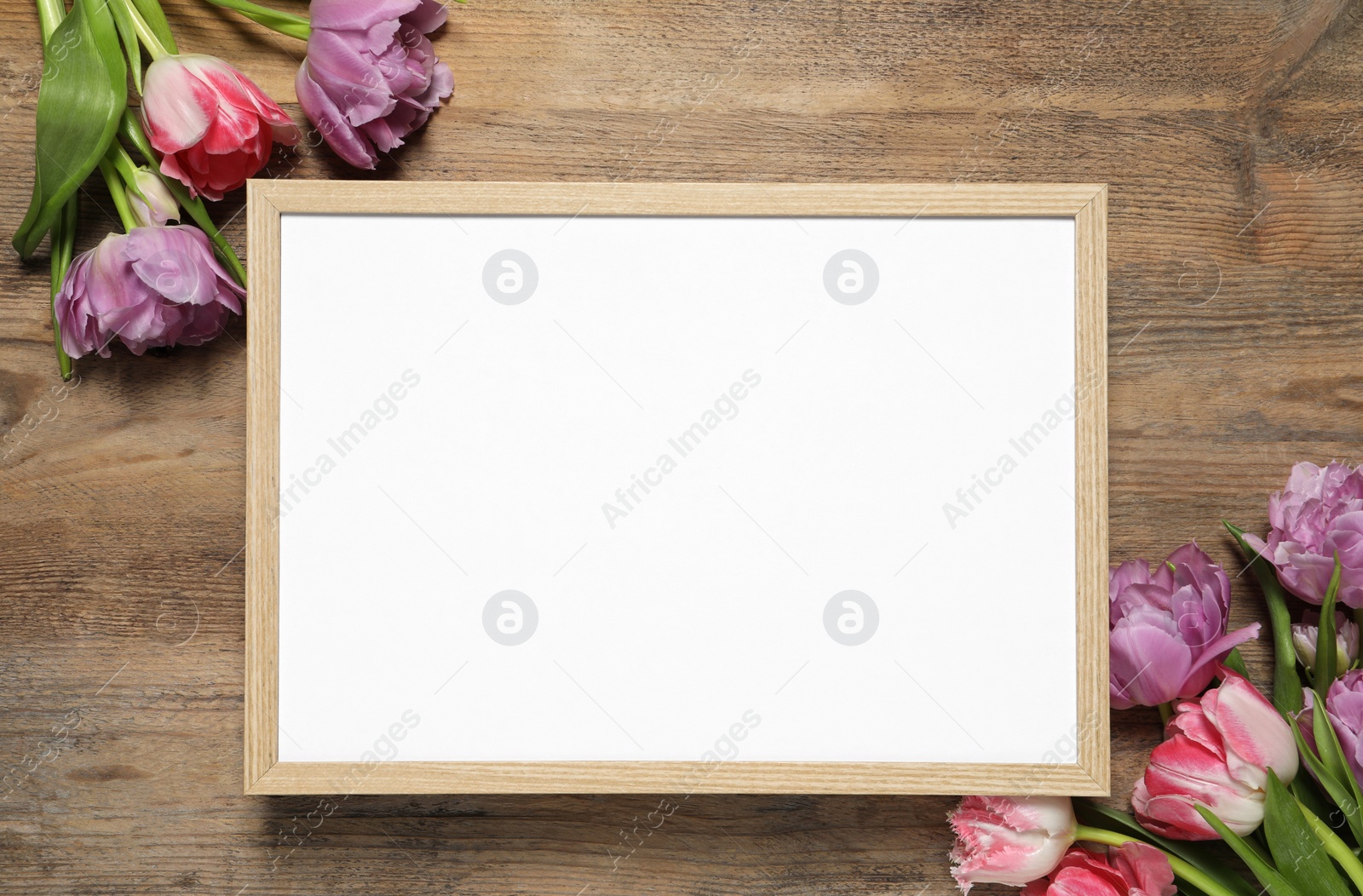 Photo of Empty photo frame and beautiful flowers on wooden table, flat lay. Space for design