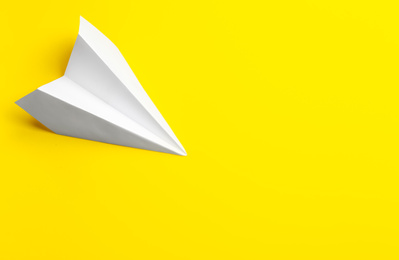 White paper plane on yellow background, top view. Space for text