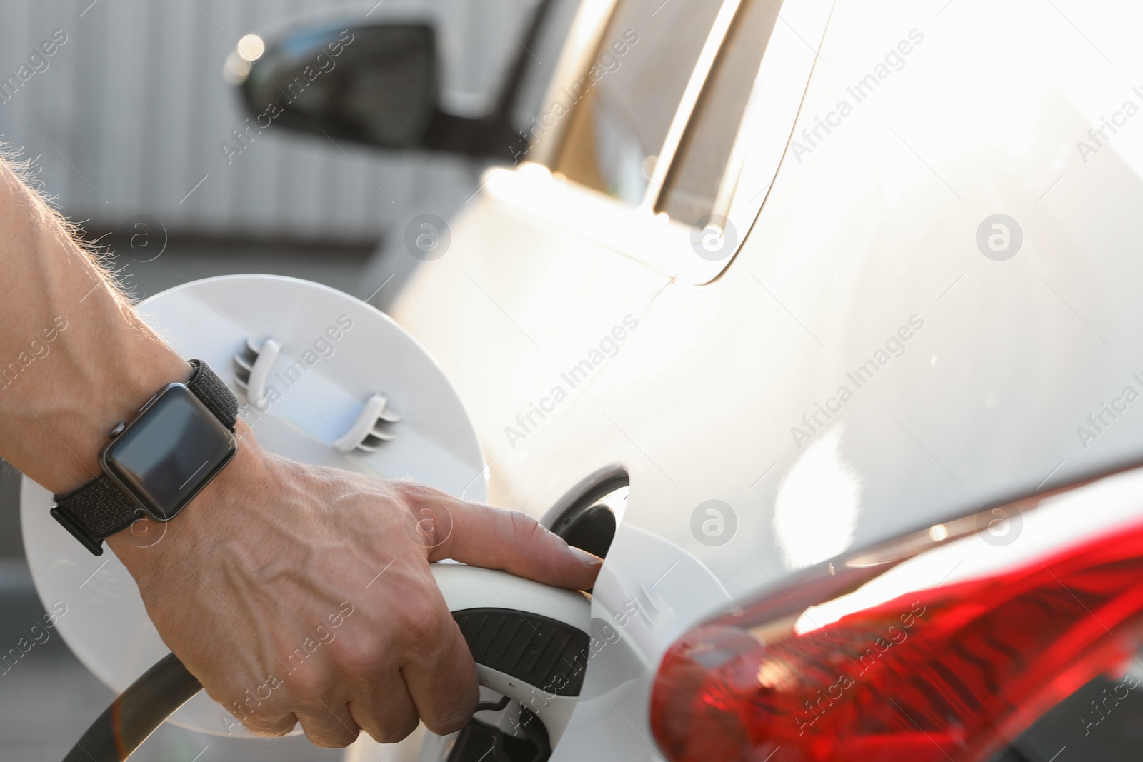 Photo of Man inserting plug into electric car socket at charging station, closeup