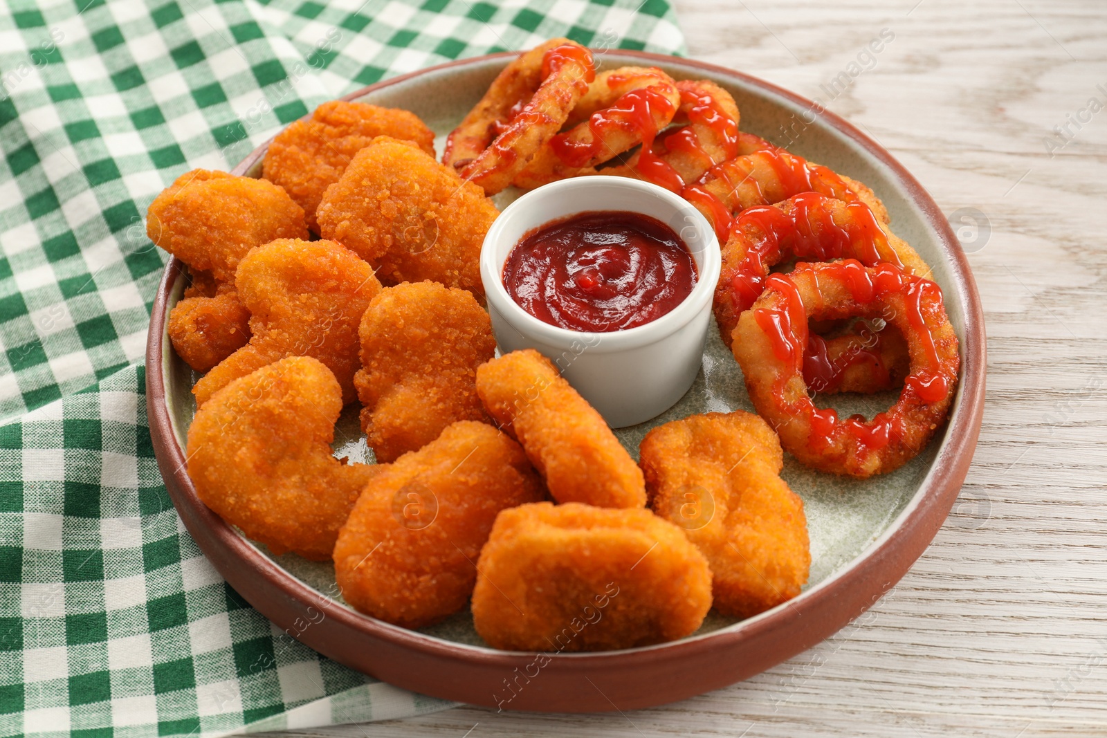 Photo of Tasty fried onion rings, chicken nuggets and ketchup on white wooden table