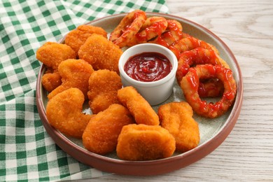 Photo of Tasty fried onion rings, chicken nuggets and ketchup on white wooden table