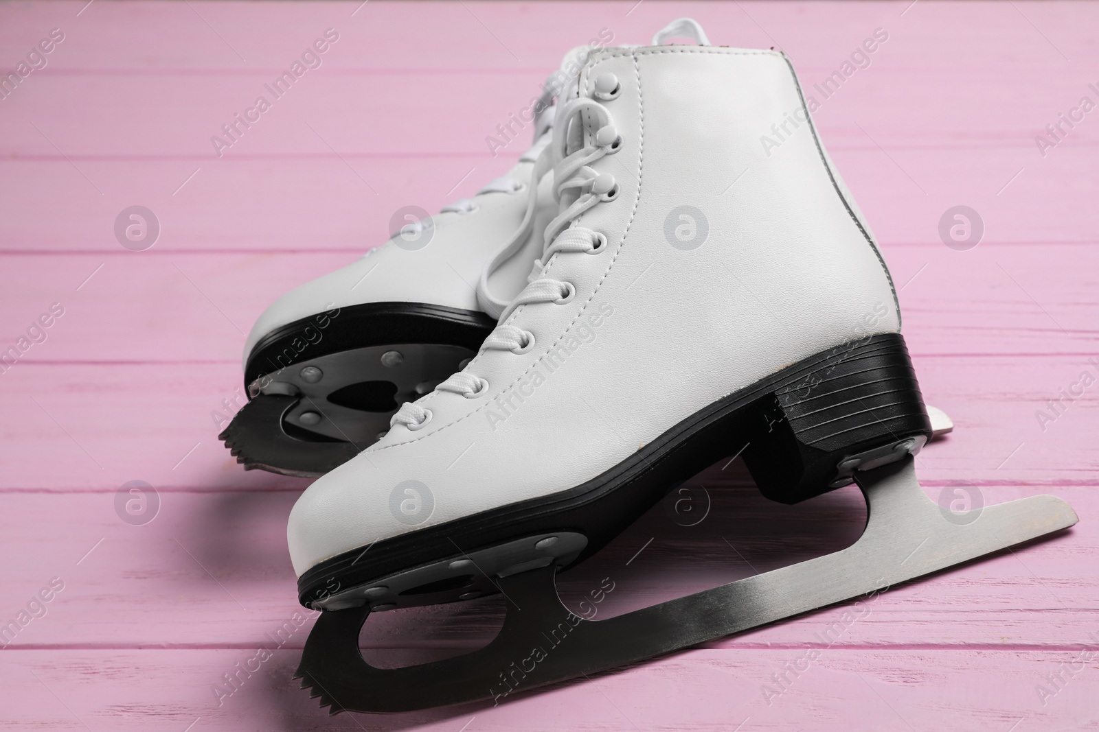 Photo of Pair of white ice skates on pink wooden table, closeup