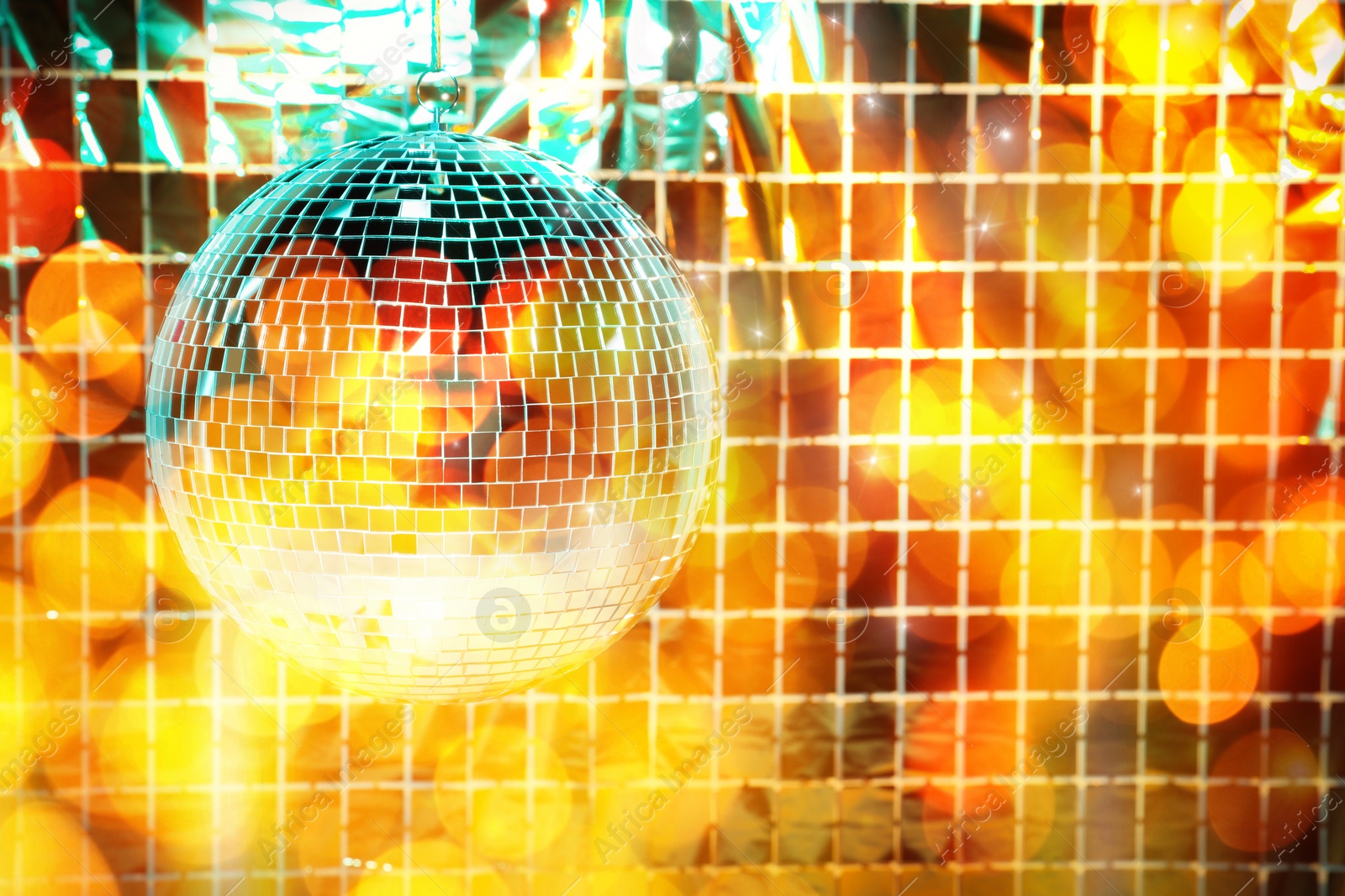 Image of Shiny disco ball against foil party curtain under golden lights, space for text. Bokeh effect