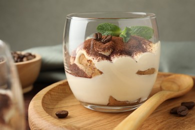 Delicious tiramisu in glass, mint leaves, coffee beans and spoon on table, closeup