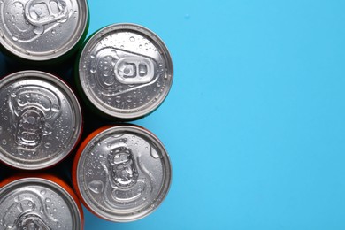 Photo of Energy drinks in wet cans on light blue background, top view. Space for text