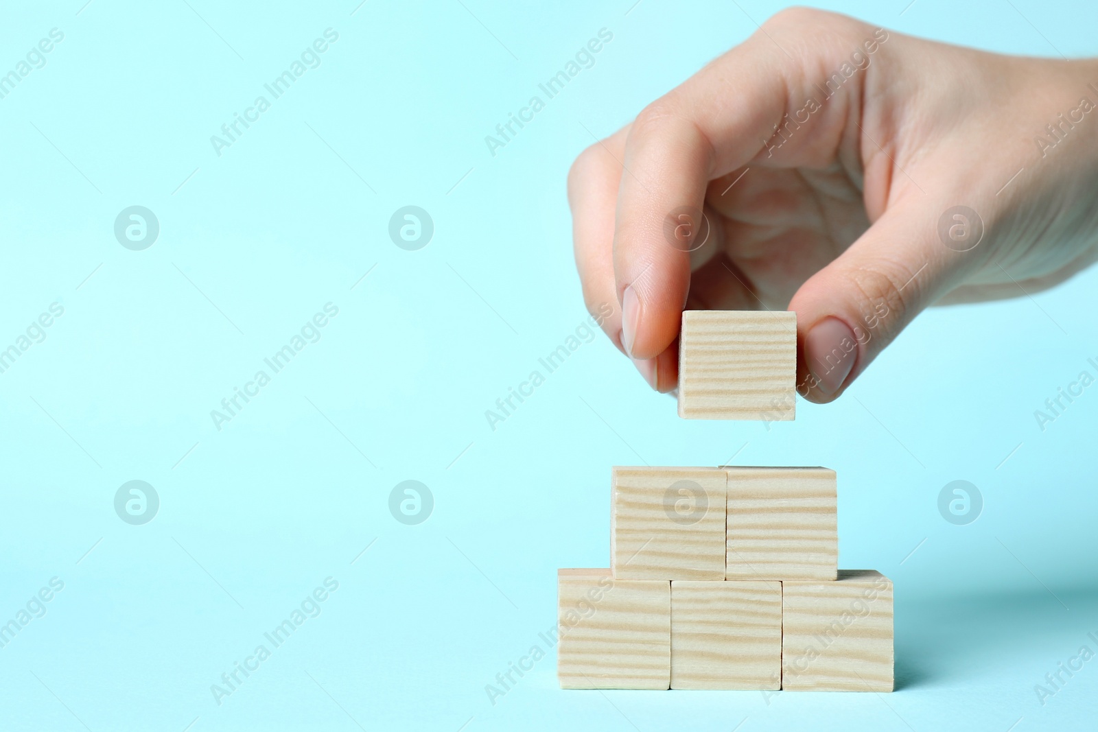 Photo of Woman building pyramid of cubes on light blue background, closeup with space for text. Idea concept