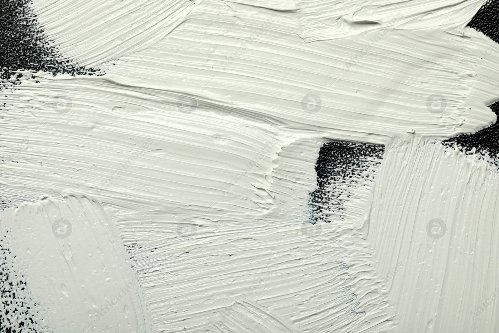 Photo of Strokes of white oil paint on black canvas, closeup