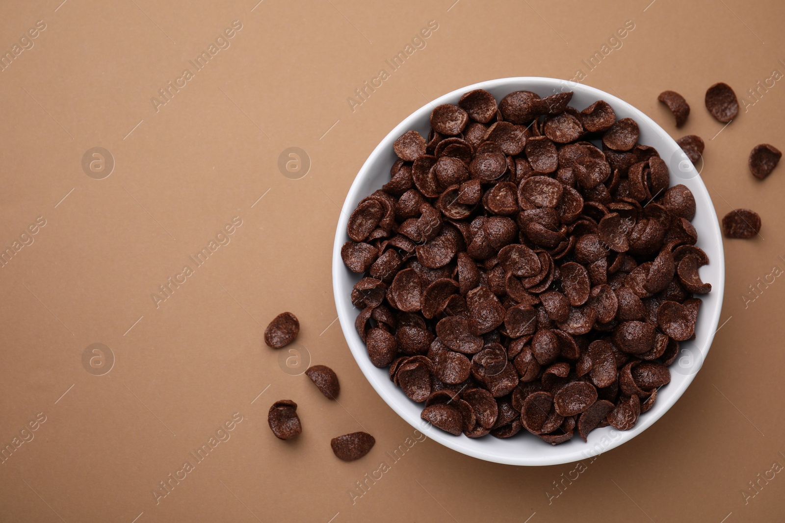 Photo of Breakfast cereal. Chocolate corn flakes in bowl on brown table, top view. Space for text