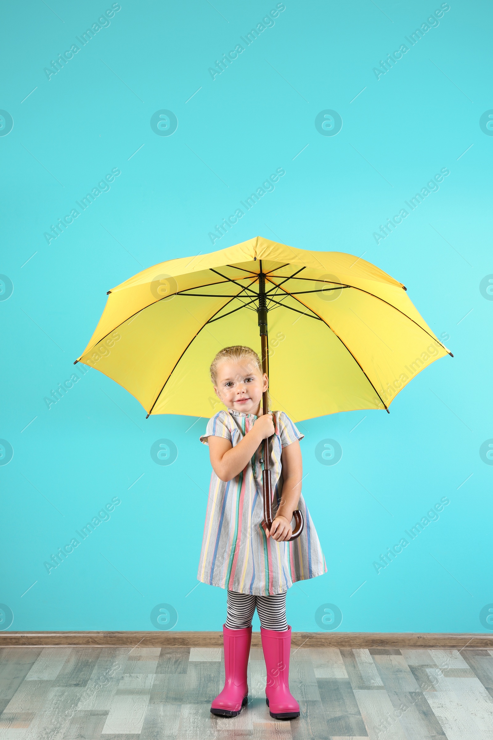 Photo of Little girl with yellow umbrella near color wall