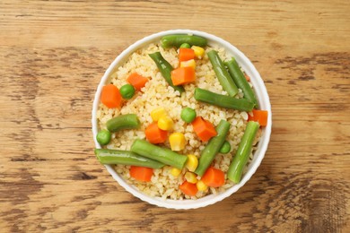 Photo of Delicious bulgur with vegetables in bowl on wooden table, top view