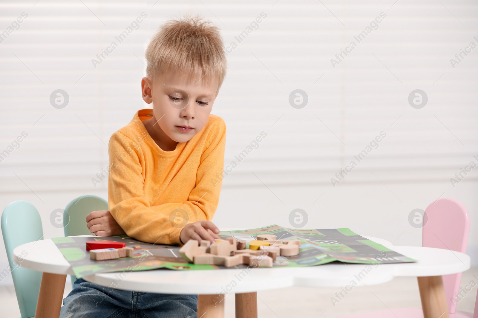 Photo of Cute little boy playing with set of wooden road signs and cars at table indoors, space for text. Child's toy