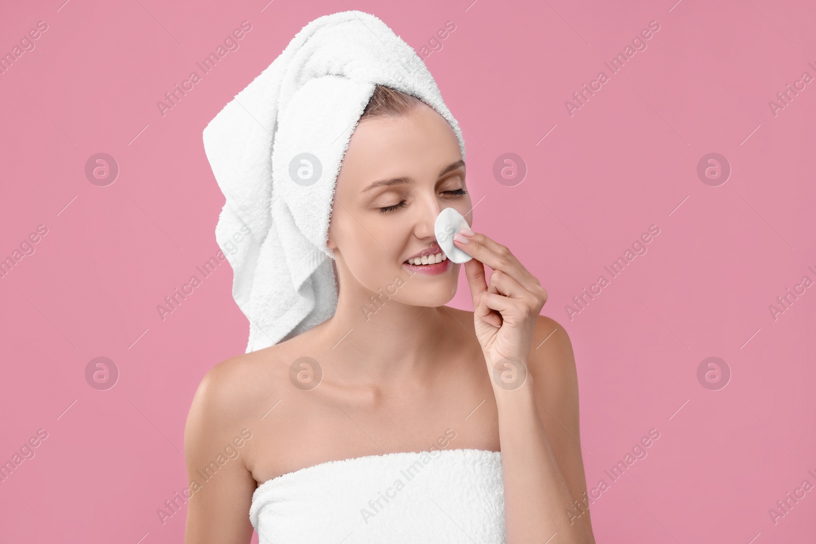 Photo of Young woman cleaning her face with cotton pad on pink background