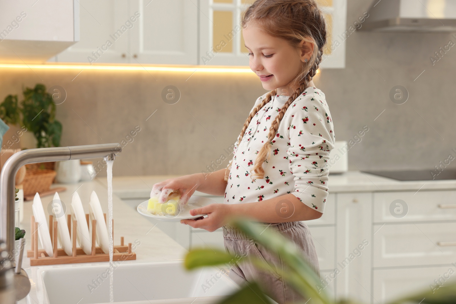 Photo of Little girl washing plate above sink in kitchen