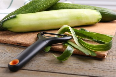 Photo of Fresh cucumbers, peels and peeler on wooden table, closeup
