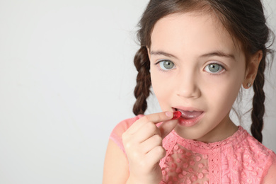 Photo of Little girl taking vitamin capsule on light background. Space for text