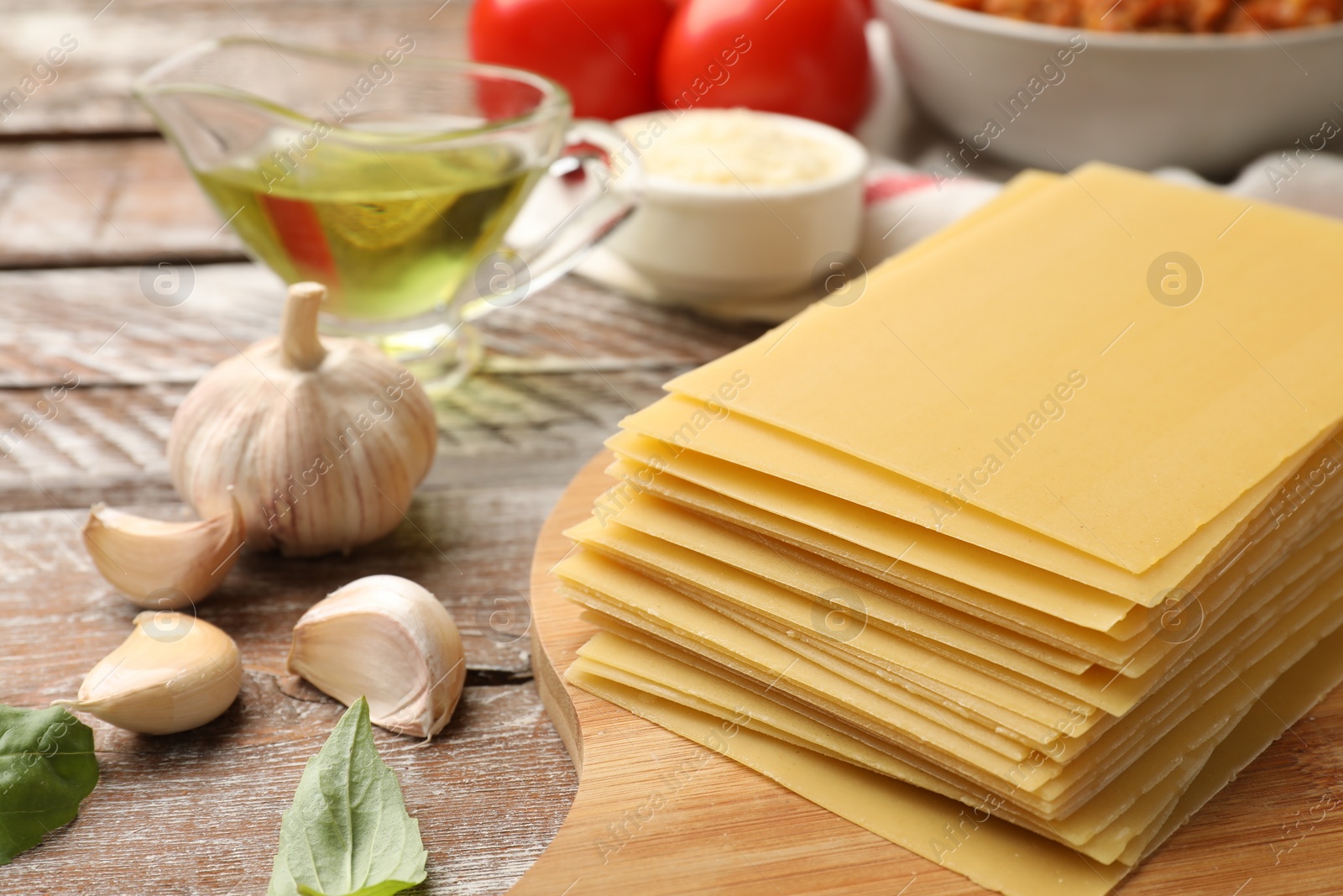 Photo of Stack of pasta sheets and other products for cooking lasagna on wooden rustic table, closeup