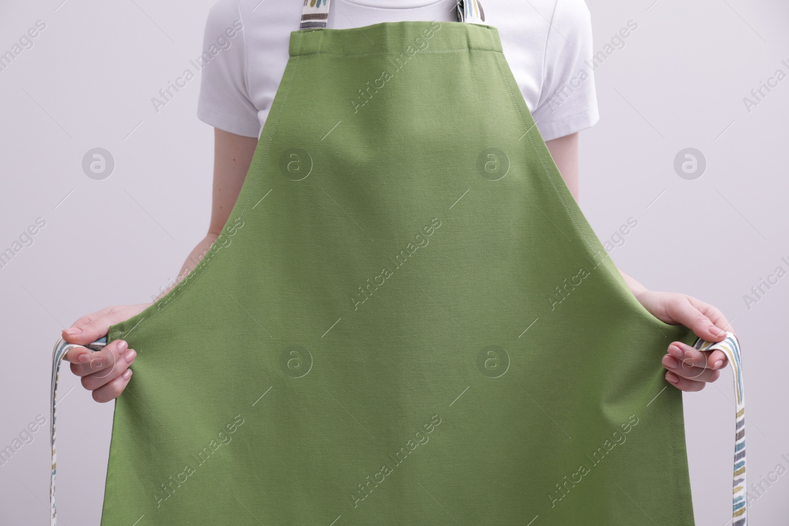 Photo of Woman putting on green apron against white background, closeup